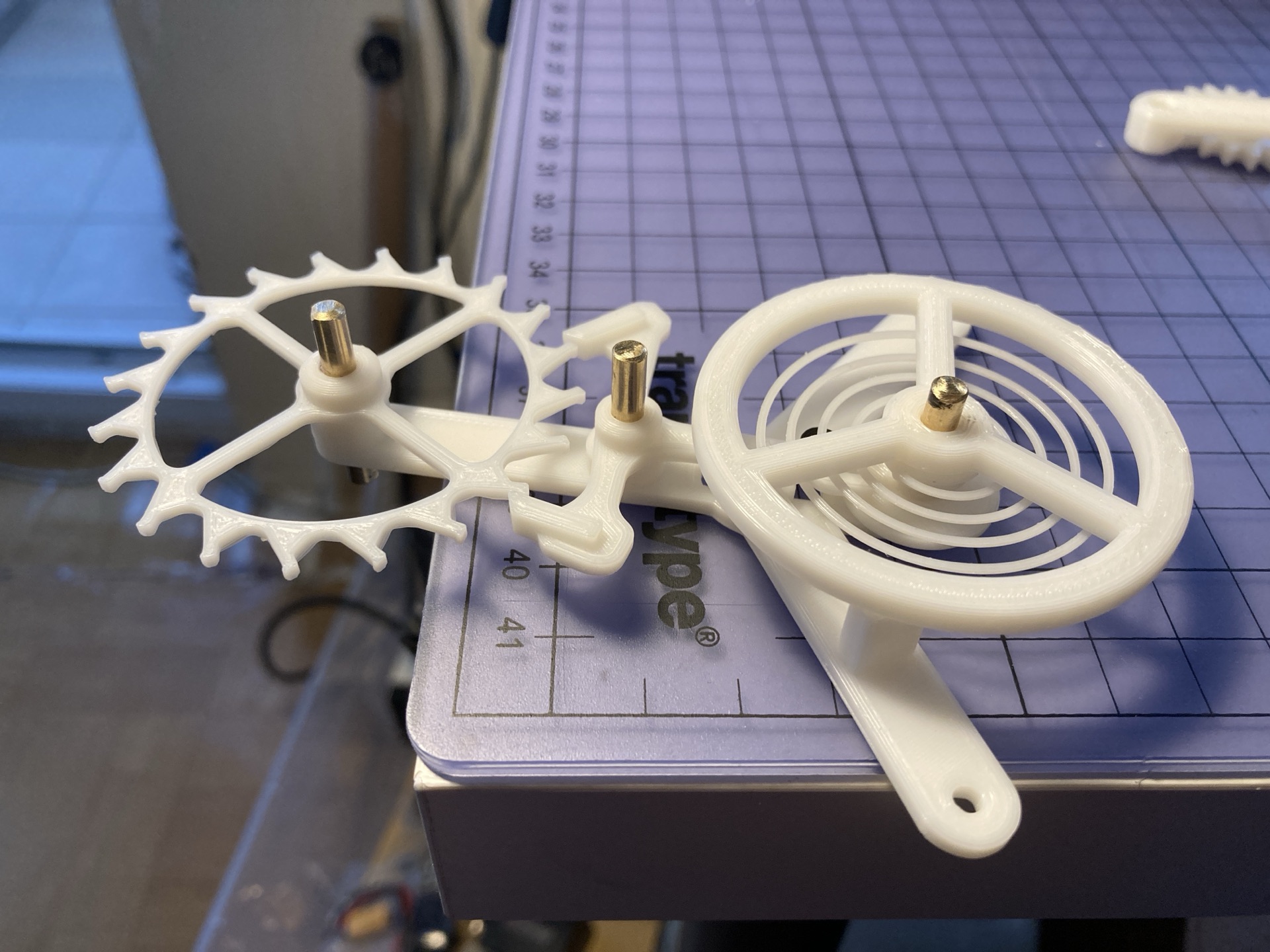 A 3D-printed mechanism with a toothed wheel and spiral spring on a cutting mat.